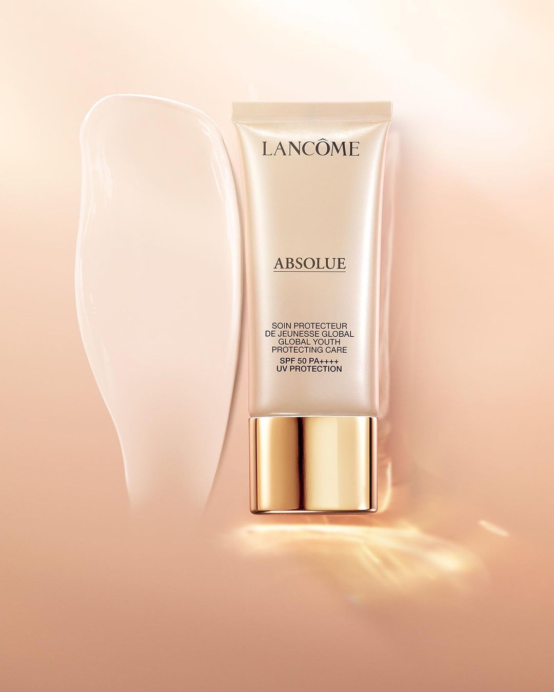 Lancôme Absolue skincare product in a tube next to a smudge of cream on a gradient peach background, product shot, beauty ad.