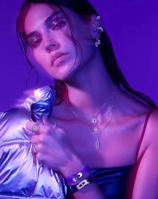 Portrait of a young adult female with dark hair and jewelry, wearing a puffer jacket in a neon violet and blue light setting.