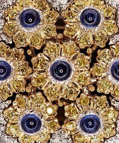 Close-up of floral-patterned gold and silver jewelry with blue gemstone centers, showcasing detailed craftsmanship and geometric arrangement.