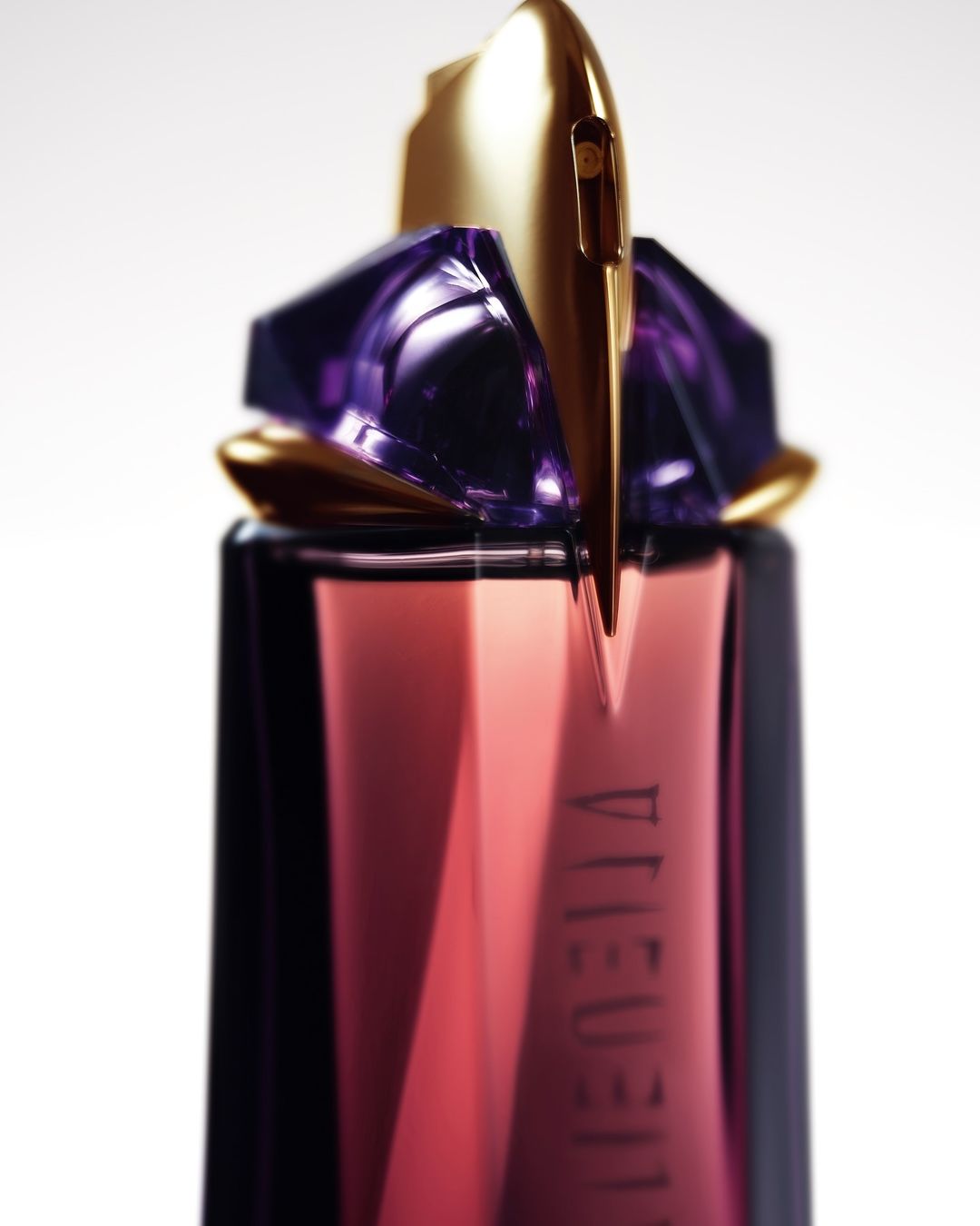 Close-up of a perfume bottle featuring geometric gold and purple shapes against a white background, suitable for beauty or fragrance advertising.