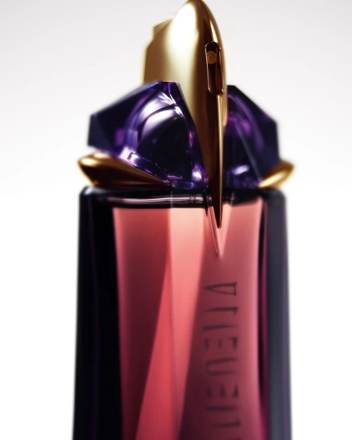 Close-up of a perfume bottle featuring geometric gold and purple shapes against a white background, suitable for beauty or fragrance advertising.