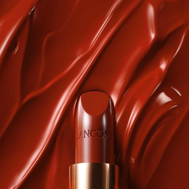 Close-up of a red Lancôme lipstick tube centered against a backdrop of textured, glossy, similar-colored makeup, glossy finish.