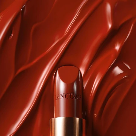 Close-up of a red Lancôme lipstick tube centered against a backdrop of textured, glossy, similar-colored makeup, glossy finish.