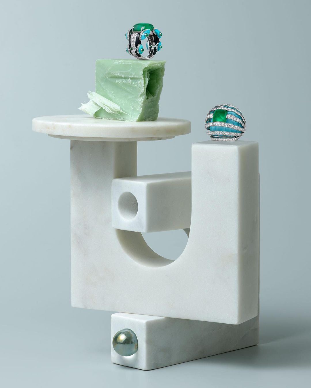 Close-up still life of two gemstone rings displayed on an abstract sculpture with geometric shapes in a softly lit, studio setting.
