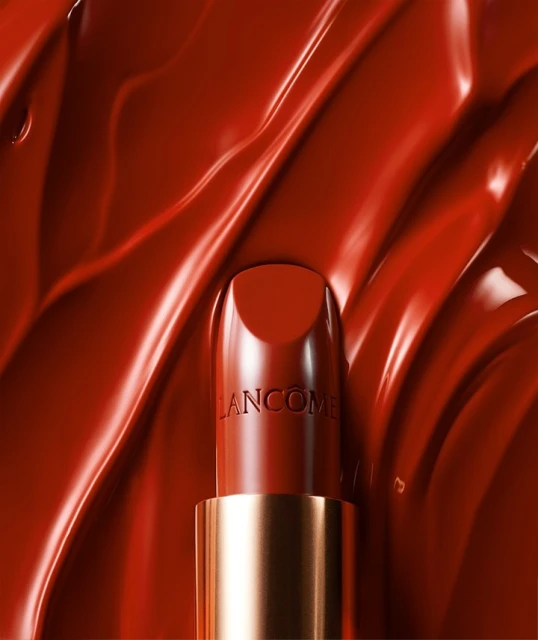 Close-up studio shot of red Lancôme lipstick with a gold tube against a backdrop of swirling red lipstick cream.