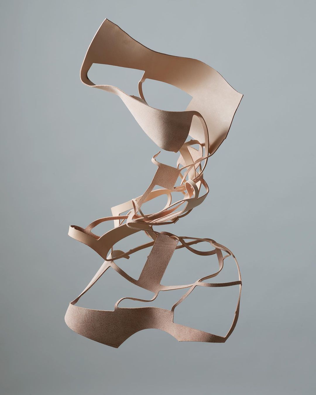 Abstract art sculpture made from layered tan leather strips suspended against a gray background, creating a surreal, textured form.