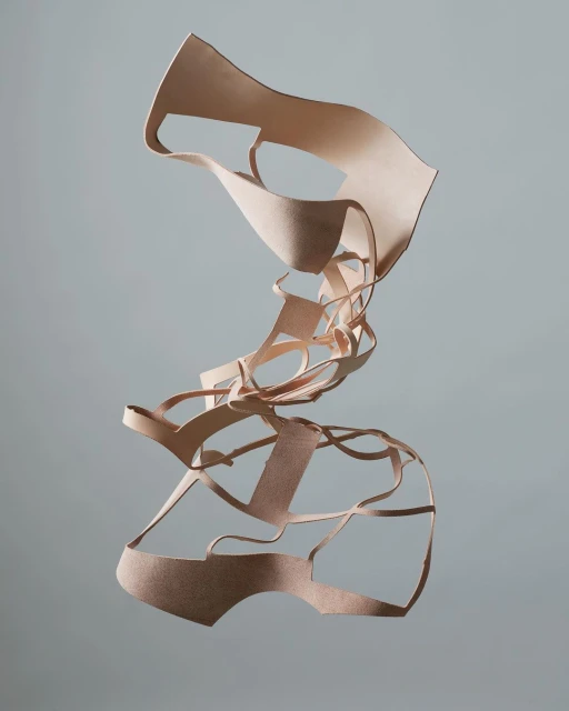 Abstract art sculpture made from layered tan leather strips suspended against a gray background, creating a surreal, textured form.