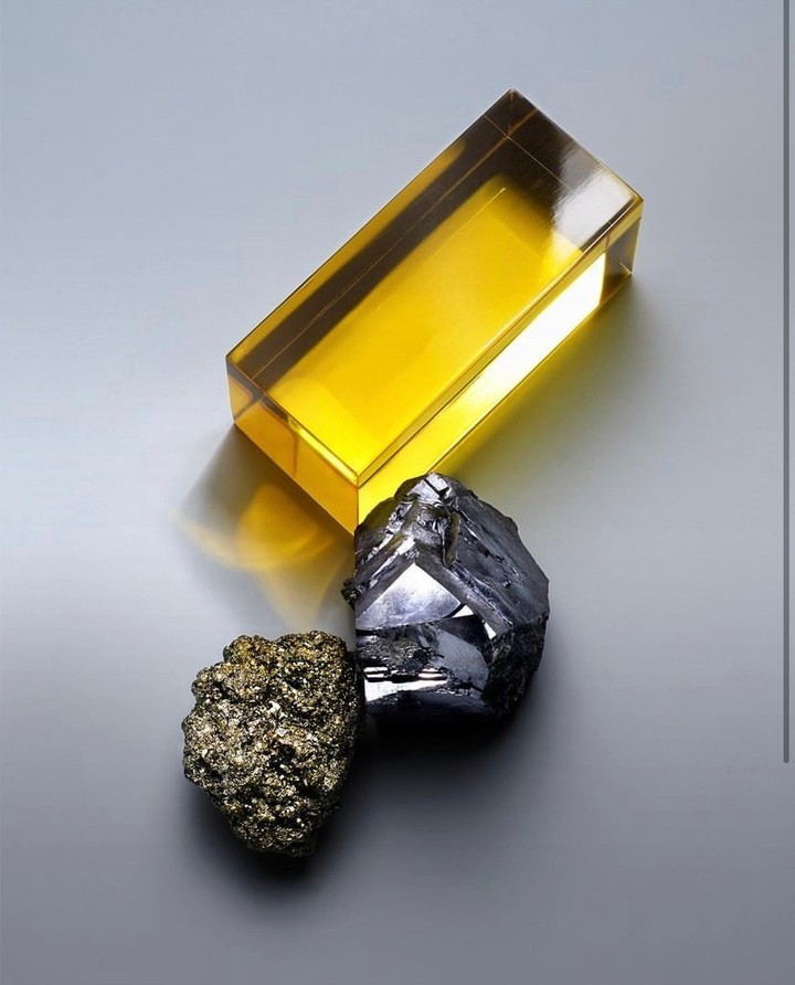 Still life shot featuring a yellow transparent block next to two rough minerals on a smooth gray surface, creating a simple yet striking composition.