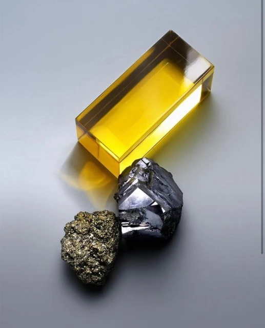 Still life shot featuring a yellow transparent block next to two rough minerals on a smooth gray surface, creating a simple yet striking composition.