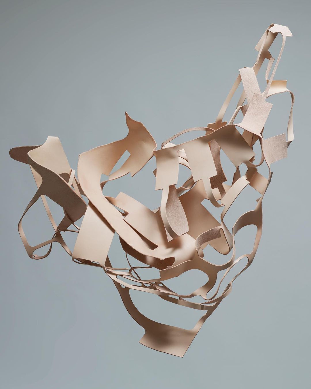 Abstract art featuring a sculptural arrangement of interconnected, cut-out shapes in neutral tones against a light grey background.