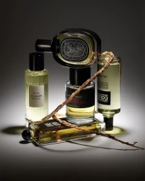 Stacked perfume bottles with pale yellow liquid against a dark gradient studio background with a dry woven twig