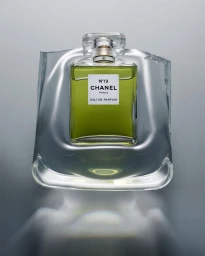 A bottle of Chanel No 19 perfume encased in clear, distorted molded plastic against a gradient grey studio background.