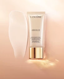 Lancome Absolue skincare product tube upright with a glossy cream swatch smear on a warm peach background.