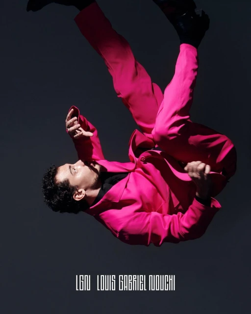 Man in bright pink suit with dark shoes poses at an angle against a dark grey background in a fashion photography studio shoot.