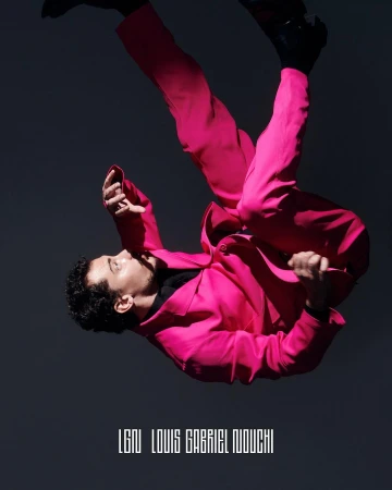 Man in bright pink suit with dark shoes poses at an angle against a dark grey background in a fashion photography studio shoot.
