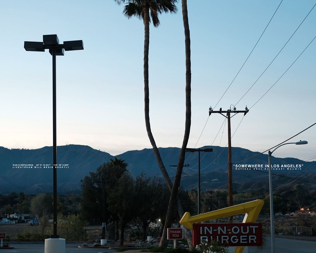 Dusk scene captures an In-N-Out Burger sign with palm trees and mountains, framed by streetlights against a twilight sky in Los Angeles.