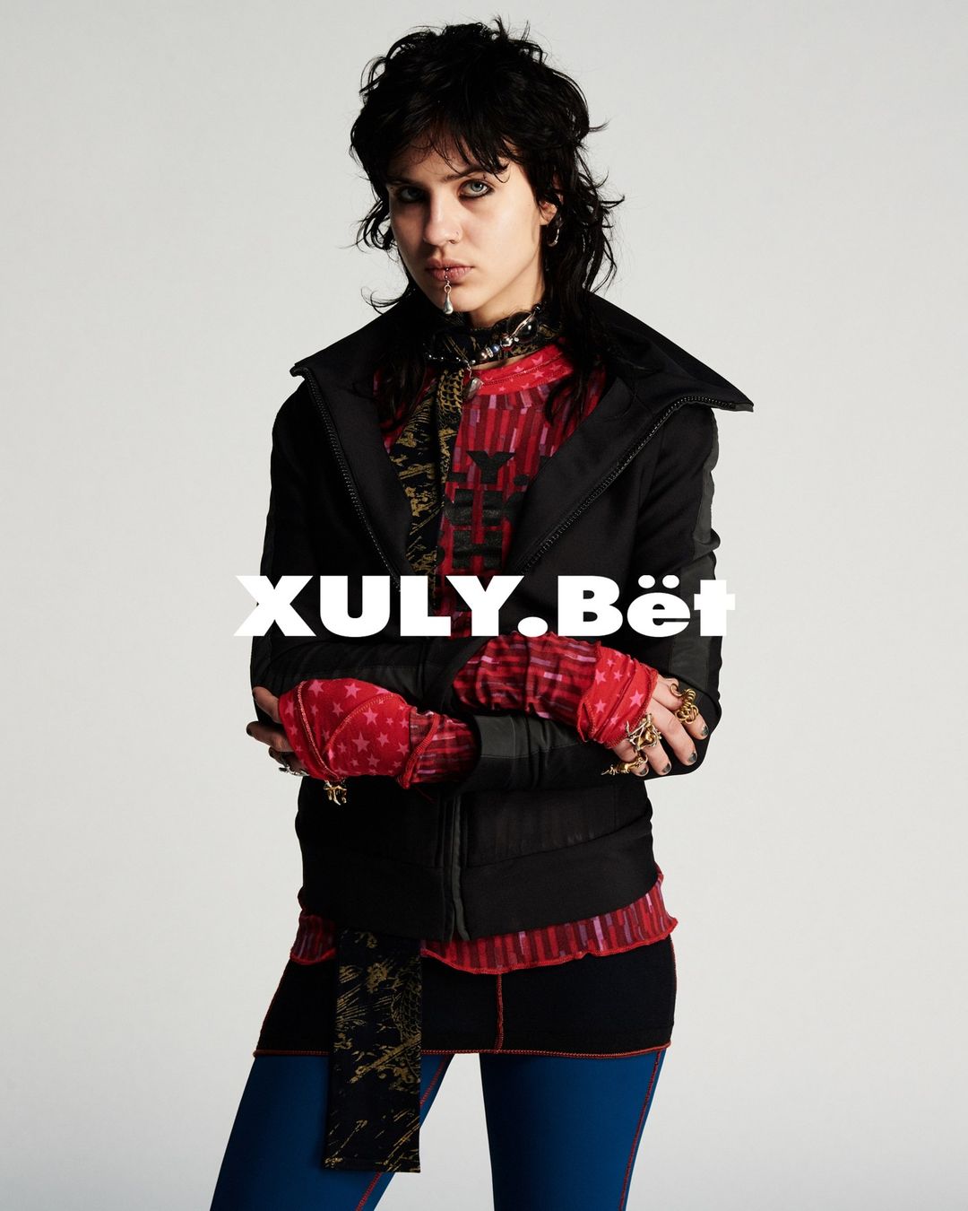 Portrait of a female adult in black jacket and leggings against a white backdrop, showcasing a fashion-forward editorial look with bold styling.