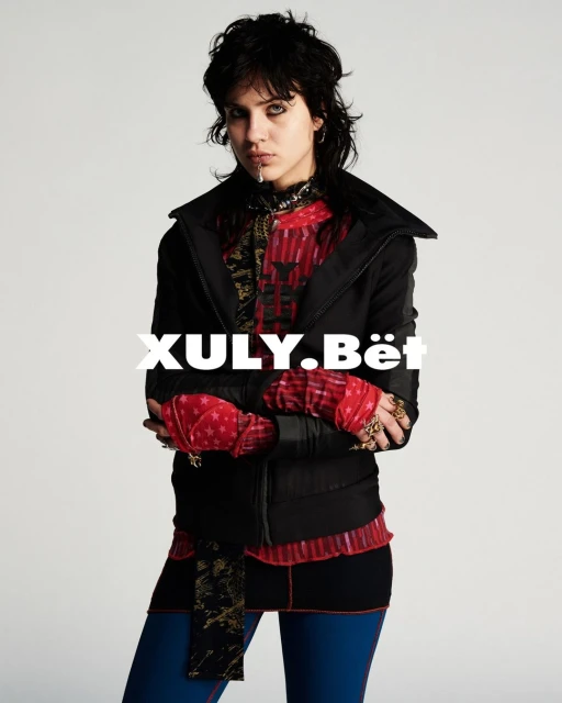 Portrait of a female adult in black jacket and leggings against a white backdrop, showcasing a fashion-forward editorial look with bold styling.