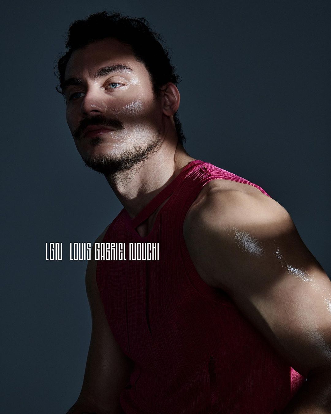 Portrait of a male model with a mustache wearing a pink tank top, captured in a photo studio with dramatic lighting.