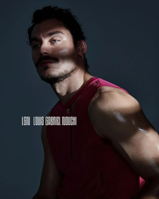 Portrait of a male model with a mustache wearing a pink tank top, captured in a photo studio with dramatic lighting.