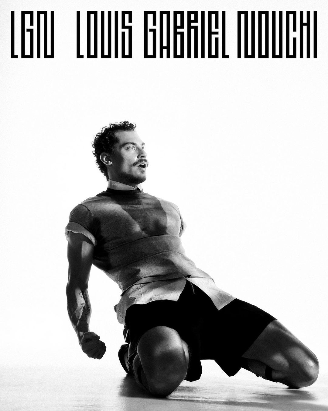 Monochromatic portrait of a muscular adult male in athletic wear on his knees with a determined expression in a brightly lit studio.