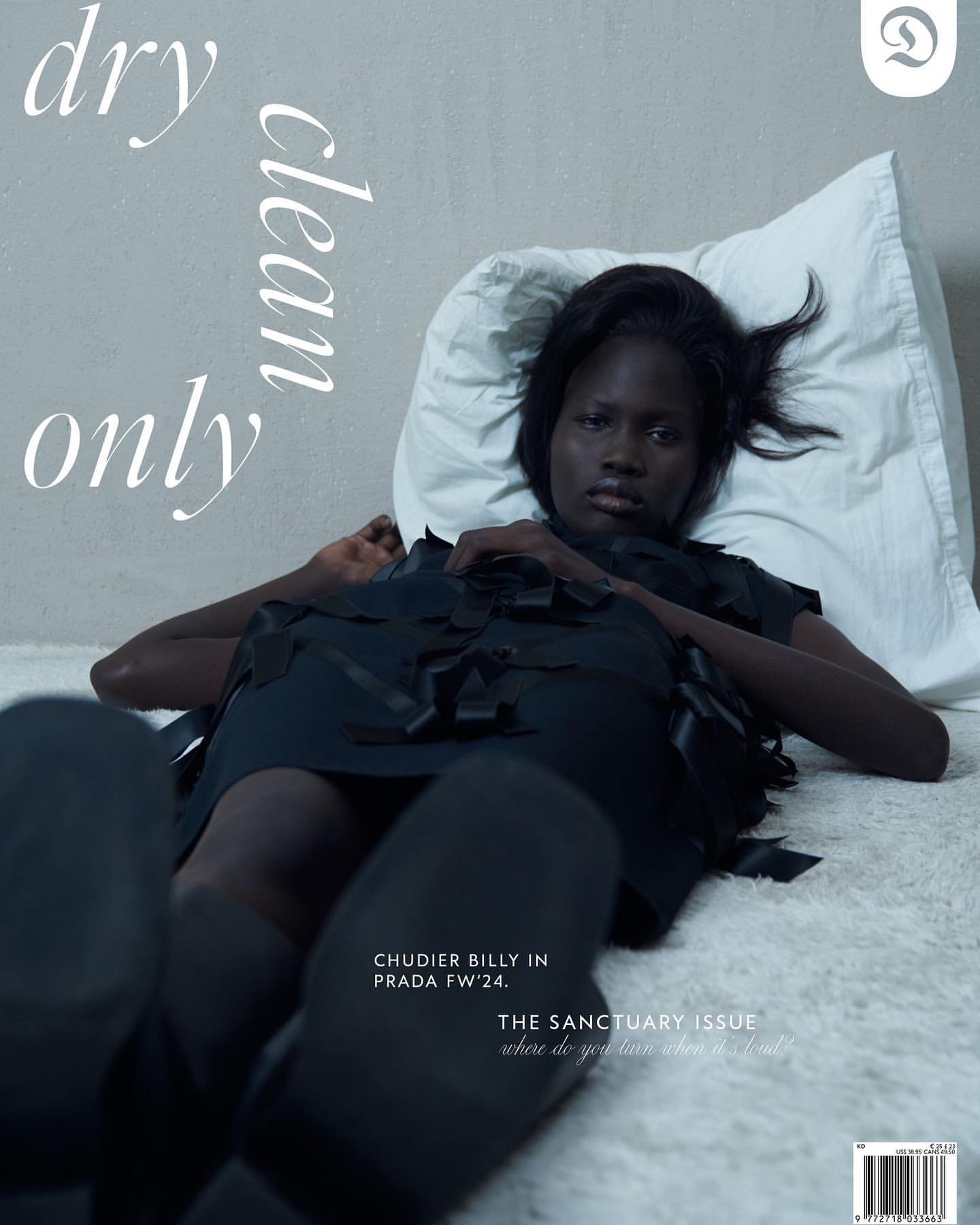 Magazine cover featuring Black female model in black dress lying on a white surface with white pillow, text overlay and fashion branding.