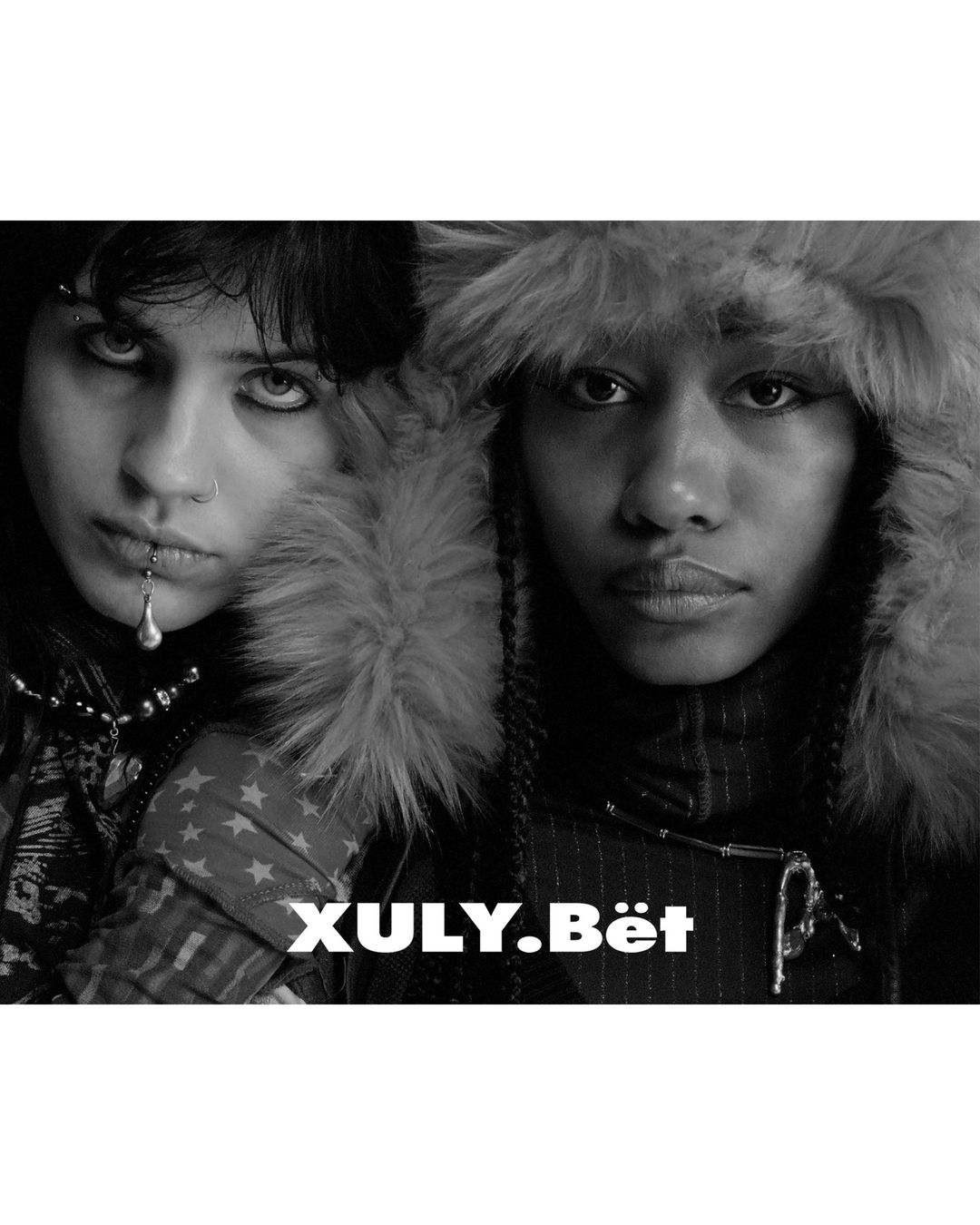 Black and white portrait of two people wearing fur-trimmed hoods and heavy clothing. The Xuly Bet logo is visible.