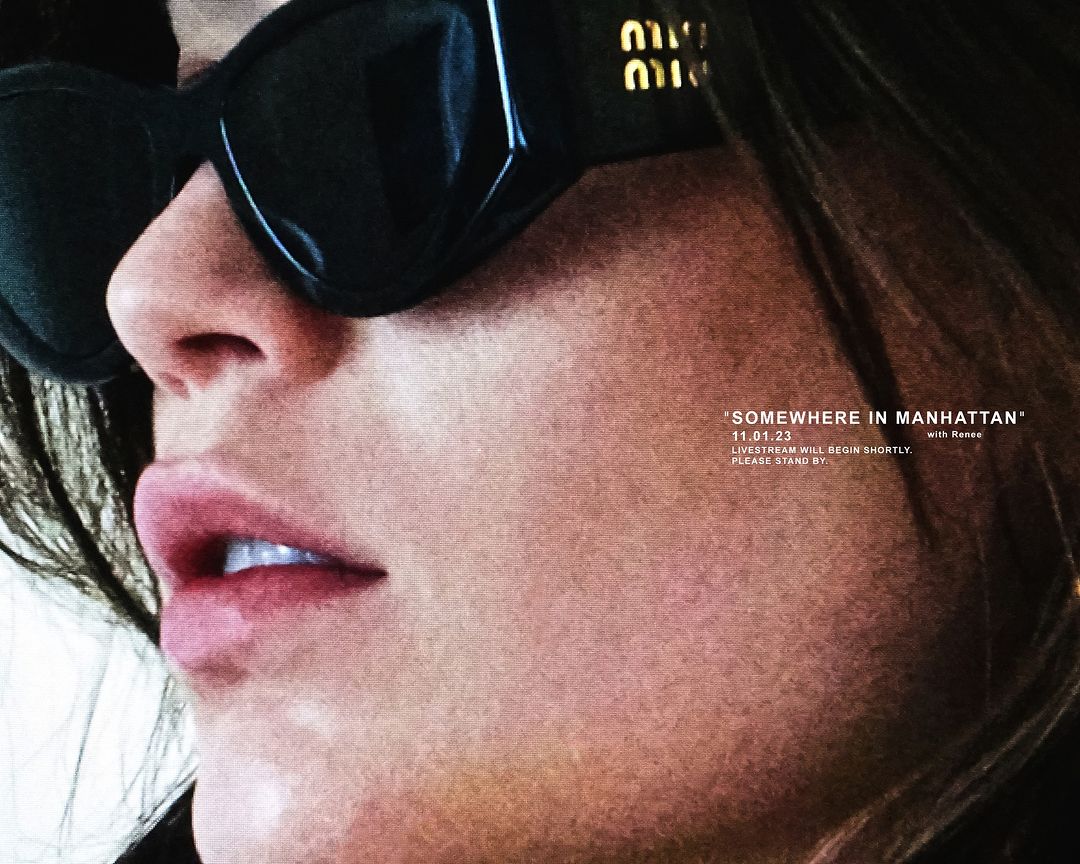 Close-up portrait of a woman wearing designer sunglasses with text overlay 'Somewhere in Manhattan', dark hair visible, soft lighting.