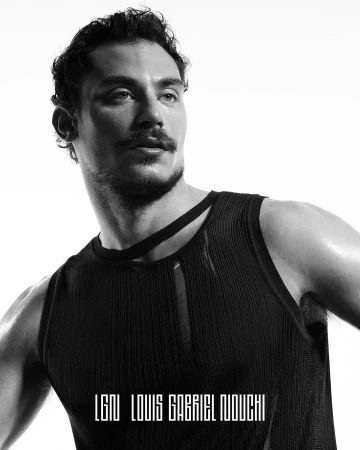 Monochrome portrait of a man in a black tank top looking away, posing against a bright white background in a studio environment.
