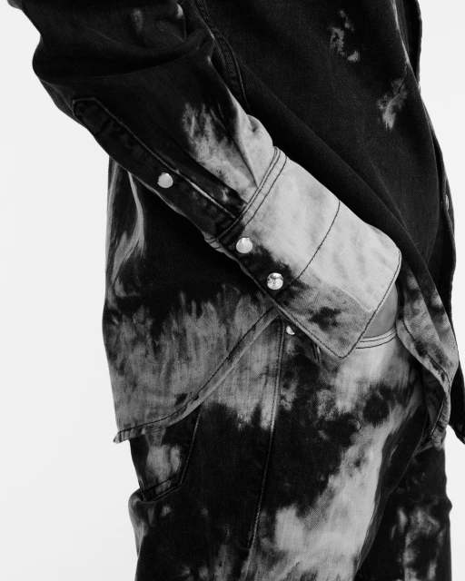 Close-up of a person wearing a black and white tie-dye denim shirt with silver buttons, showcasing the garment's texture and design.