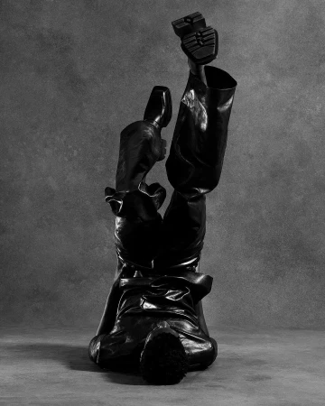 Monochrome fashion shot of a figure in shiny black trousers and boots doing a handstand against a mottled grey background.
