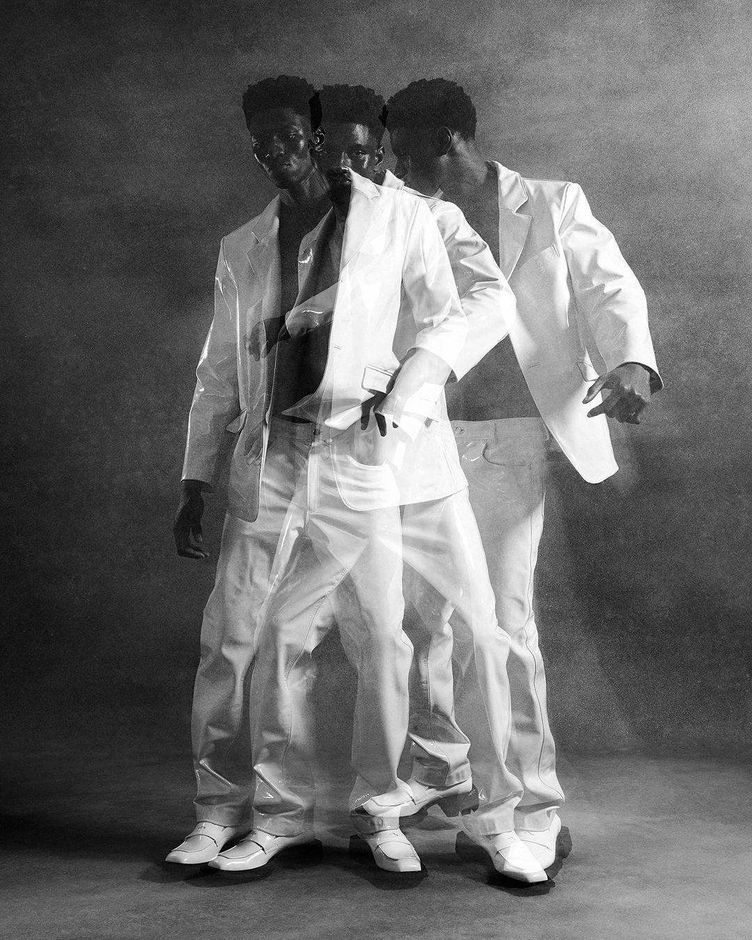 Monochrome studio shot of a Black male model in motion, wearing an unbuttoned white suit with multiple superimposed exposures.