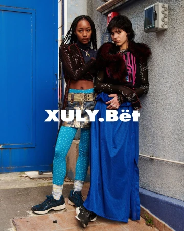 Two stylish adult women pose outdoors in fashionable clothing featuring faux fur, unique leggings, skirts, and sneakers in an urban setting.