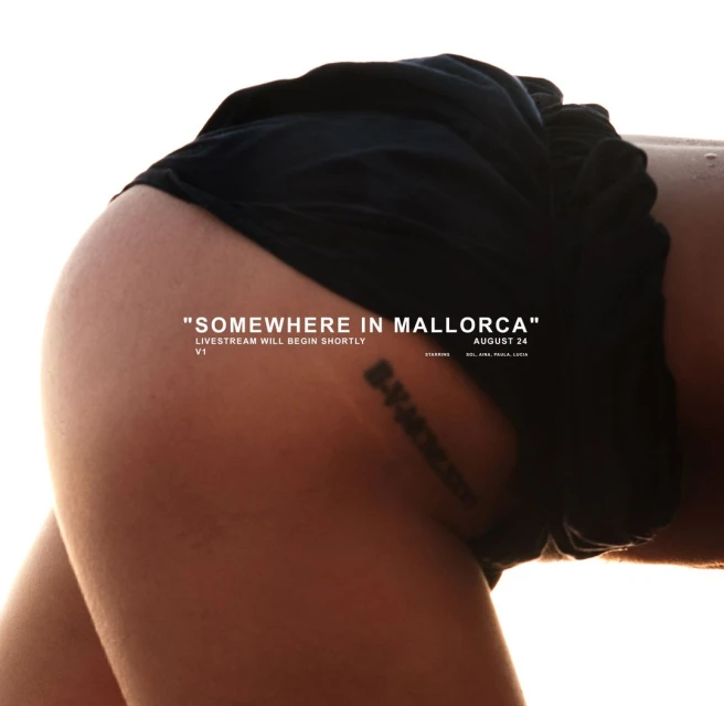 Close-up studio shot of a woman's lower back and upper thighs, featuring tanned skin, a tattoo, and black shorts against a bright background.