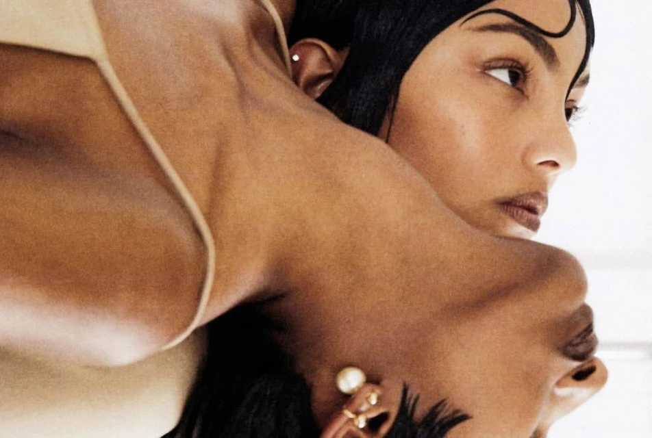 Close-up beauty shot featuring two dark-skinned adult women with dark hair in front of a bright white background. Fashion studio shot.