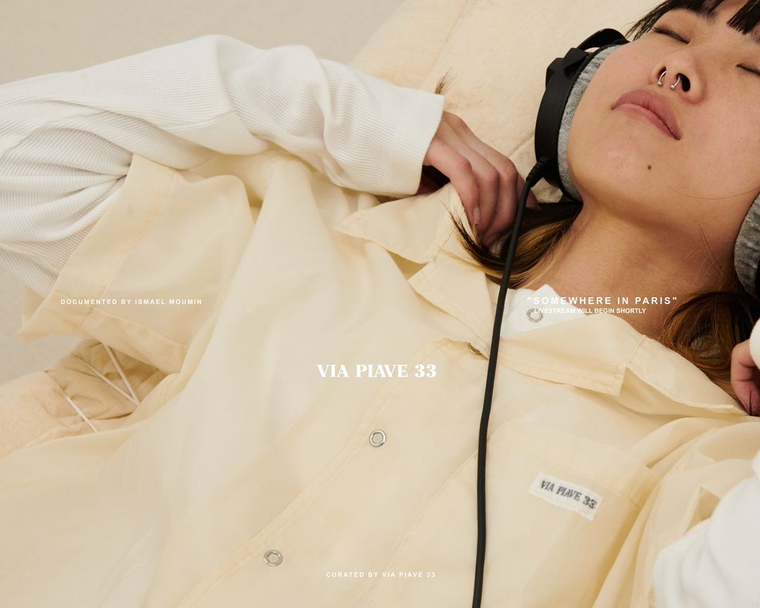 Woman with headphones rests with a yellow sheer shirt, photographed indoors with soft lighting and muted color palette. Fashion editorial.
