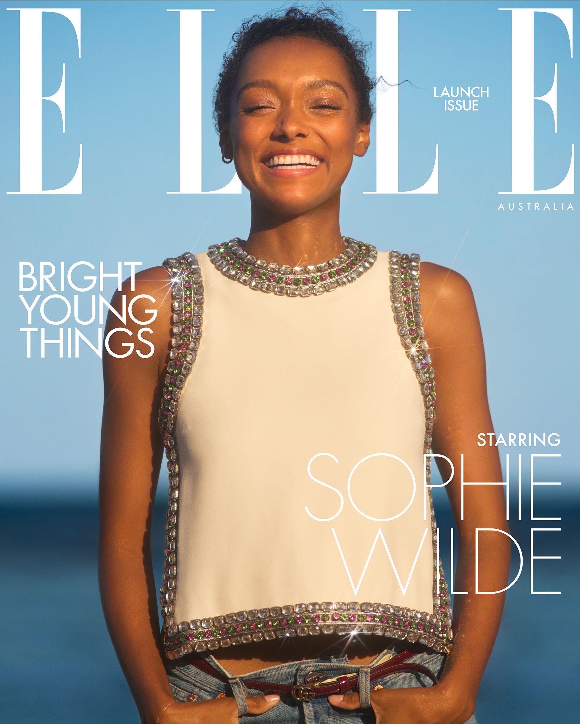 Elle Australia magazine cover featuring model Sophie Wilde. She is smiling, wearing an embellished top and jeans, against a blue sky.