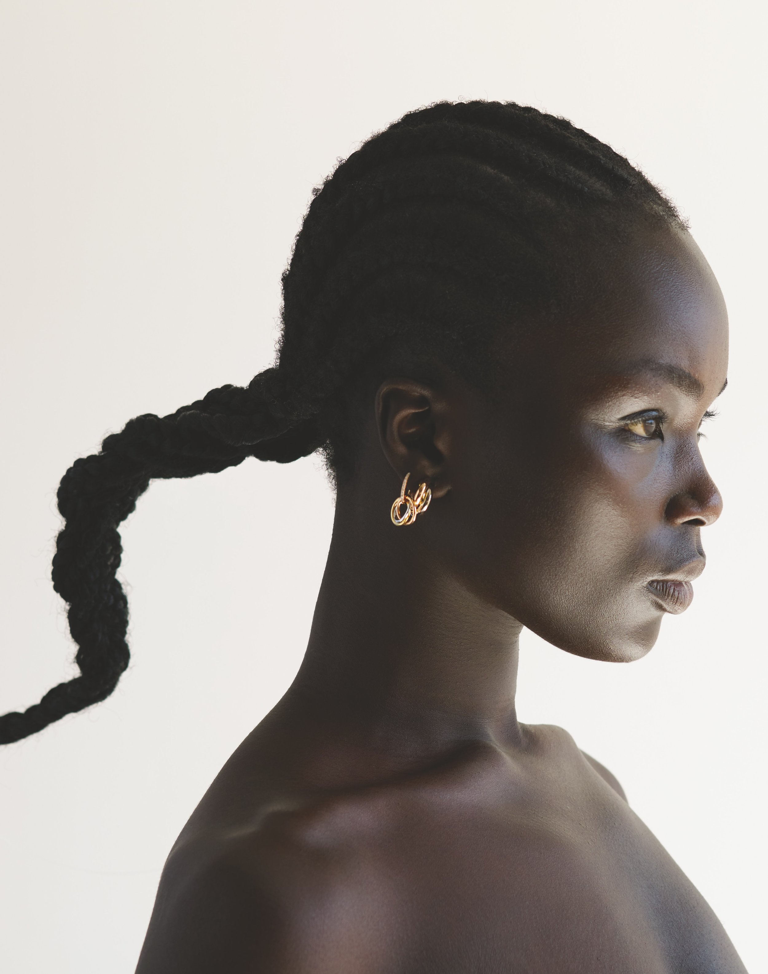 Close-up profile shot of a dark-skinned woman with braided hair and gold hoop earrings against a clean white background.