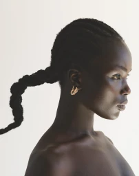 Profile portrait of a black woman with braided hair and gold hoop earrings against a bright white background