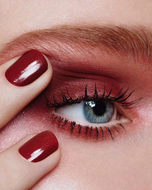 Close-up shot of a woman's blue eye with red eyeshadow and manicured fingernails framing the corner, highlighting beauty and detail.