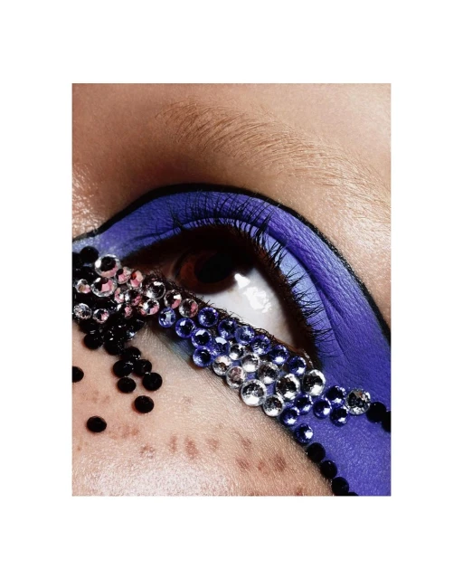 Close-up of woman's eye with blue eyeshadow and jewel embellishments. Makeup and beauty concept for cosmetics and creative artistry.