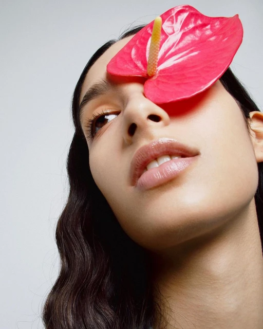 Close-up of a woman's face partially covered by a vibrant pink Anthurium flower, showcasing beauty and minimalist aesthetics.