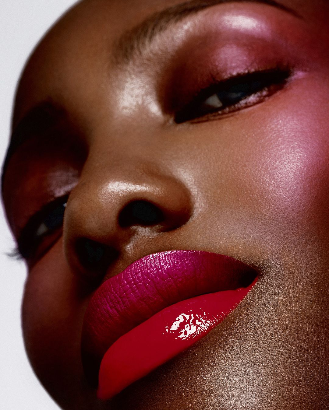 Close-up studio shot of a Black woman with pink eyeshadow and vibrant red lipstick, showcasing beauty and cosmetics, portrait orientation.