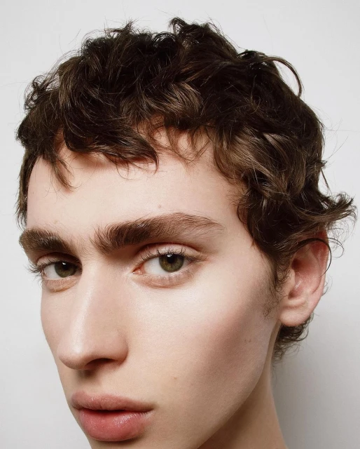 Close-up portrait of a young adult male with curly dark brown hair and fair skin, captured with shallow depth of field and studio lighting.