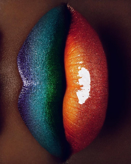 Close-up shot of brightly colored lips featuring a split design of rainbow hues and contrasting shades of orange and red.