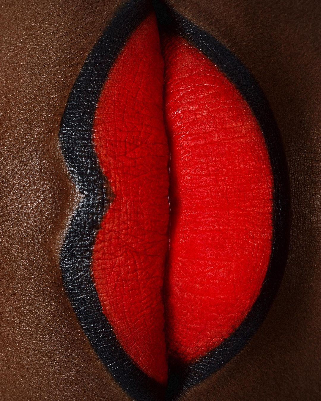 Close-up of a woman's lips with bright red lipstick and a black lip liner, creating a bold and dramatic makeup look.
