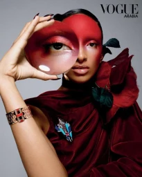 Model holding a circular mirror reflecting her eye, wearing burgundy velvet and red facial paint for Vogue Arabia.