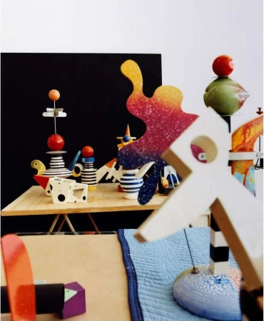 Still life photography of a collection of colourful geometric wooden objects arranged on a table with a black and white background.