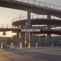 Multilevel concrete parking ramp structure at dusk with visible ramps, chain link fence, and road bollards.