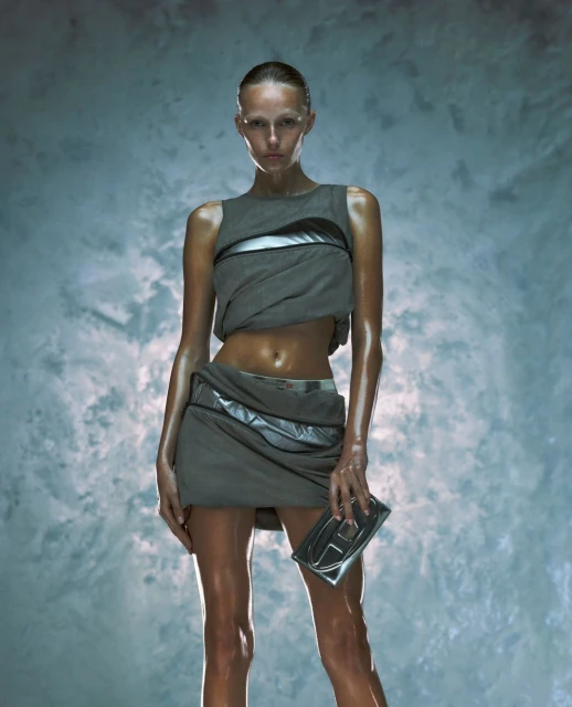 A lone adult female model, wearing a gray futuristic-style outfit and holding a clutch, is the primary focus against a textured background.